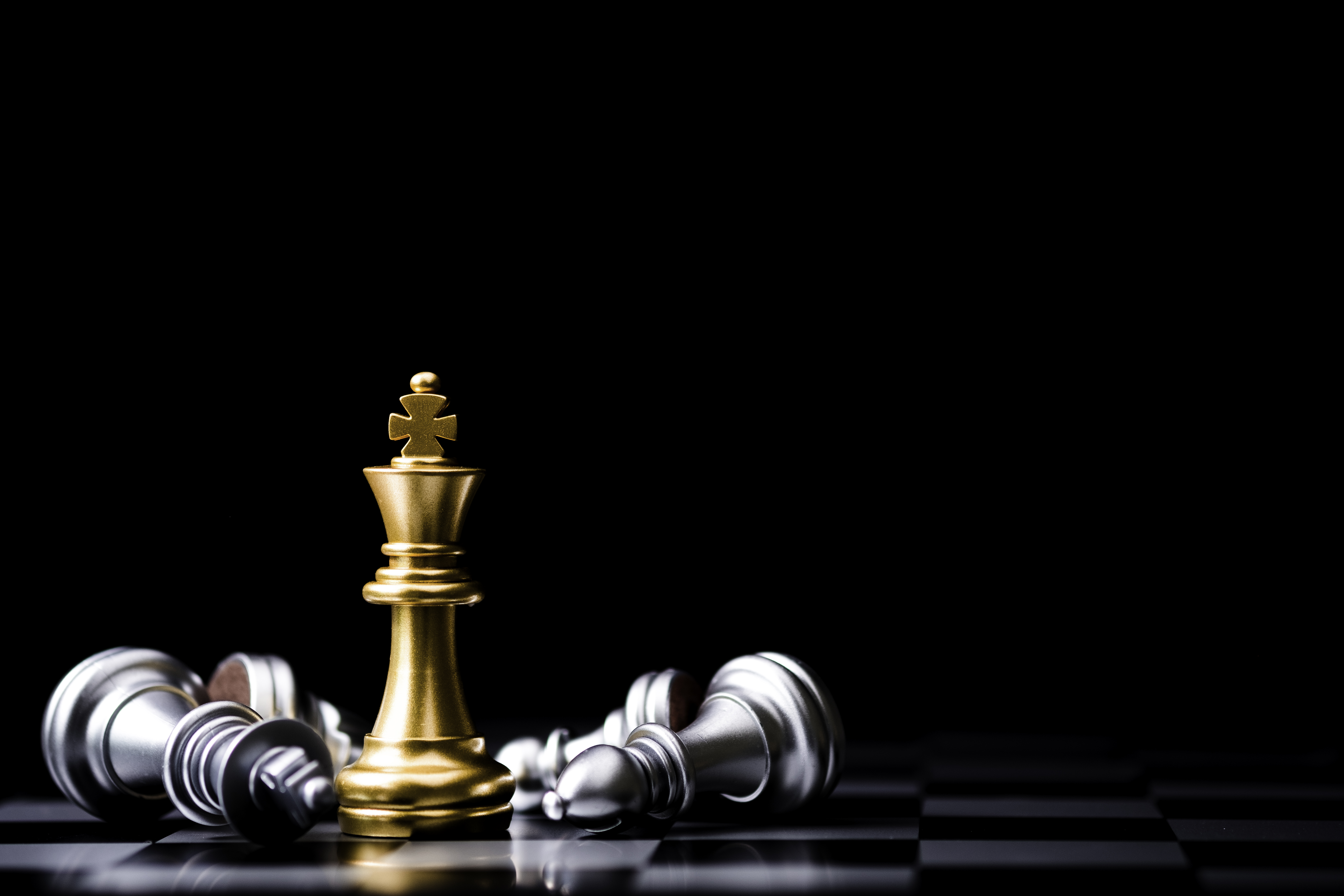 Golden king chess piece standing among fallen silver pieces — symbolizing strategic victories